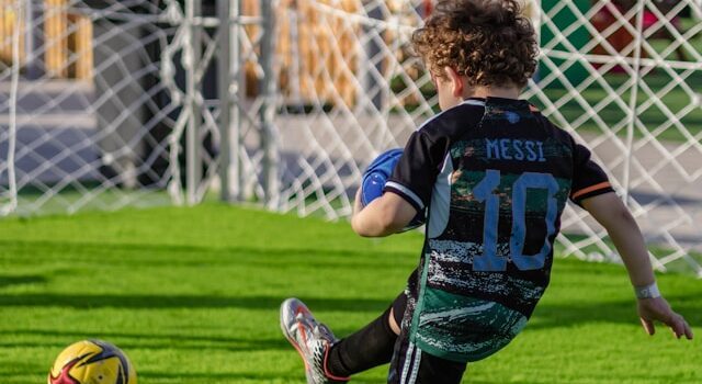 Child in Jersey kicking soccer ball into net
