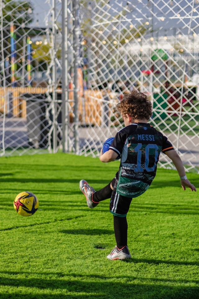 Child in Jersey kicking soccer ball into net